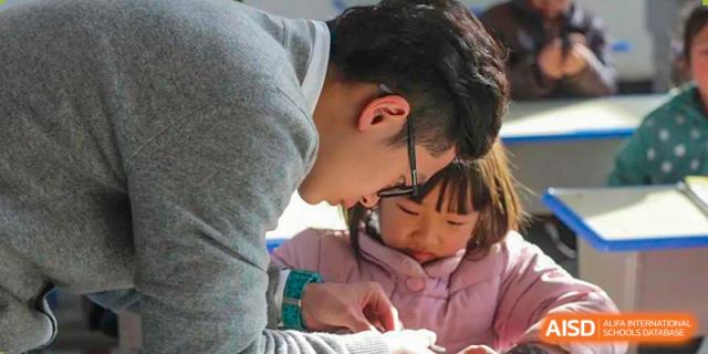 A teacher from Guangdong Country Garden School helps a young female student with her homework in a classroom.