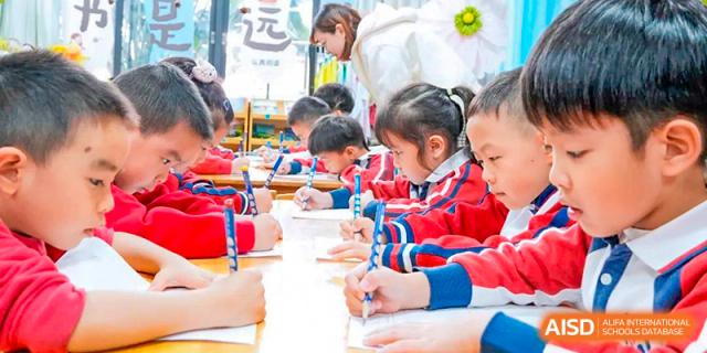Young students from Guangdong Country Garden School in red and white uniforms sit at a table and work on an art project.