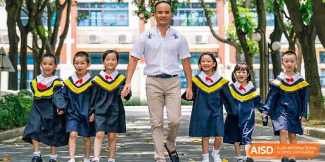 A teacher from Guangdong Country Garden School holds the hands of two young students in school uniforms.
