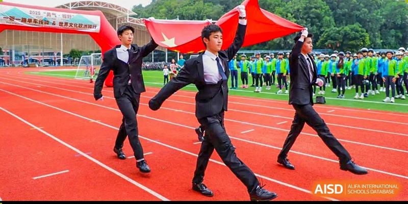 A male student from Guangdong Country Garden School in a suit holds a large Chinese flag while walking on a running track during a school event.