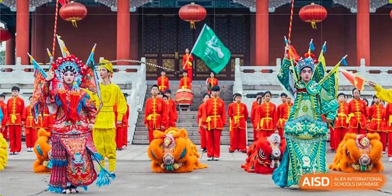 Students from Guangdong Country Garden School in red traditional outfits performing a lion dance and drumming during a cultural event.