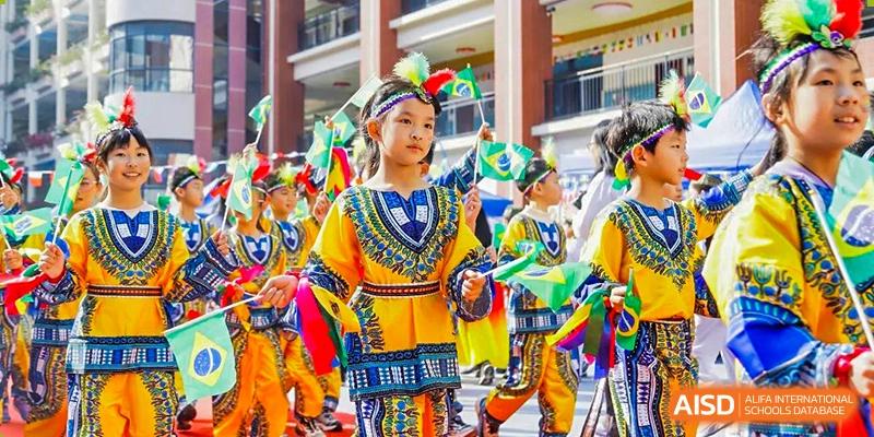 Young students from Guangdong Country Garden School in colorful, traditional folk costumes carry flags during a parade or performance.