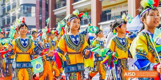 Young students from Guangdong Country Garden School in colorful, traditional folk costumes carry flags during a parade or performance.