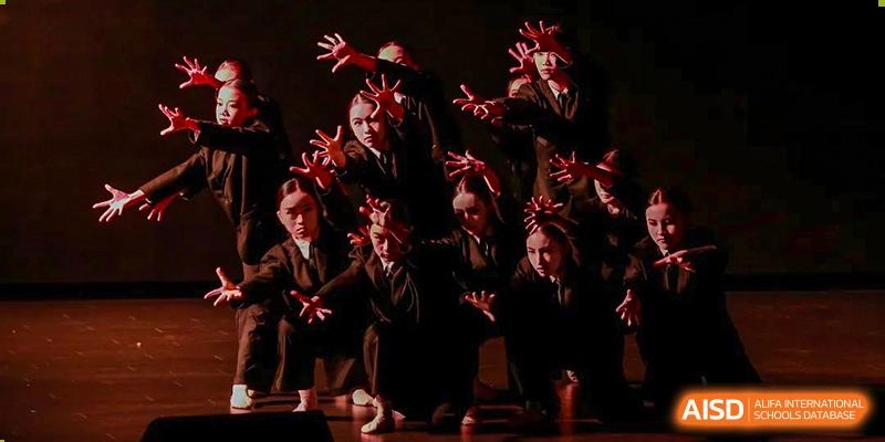 A group of students from Guangdong Country Garden School in dark suits and red ties performs a dramatic dance with outstretched hands on a stage.