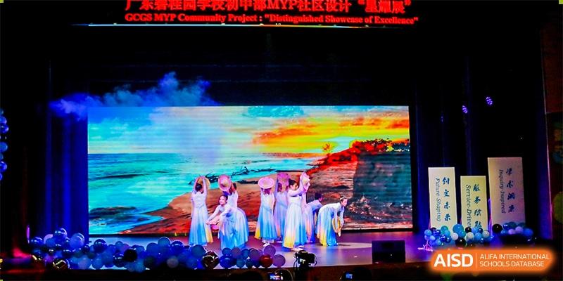 Students from Guangdong Country Garden School perform a dance on a stage with a brightly colored, abstract background.