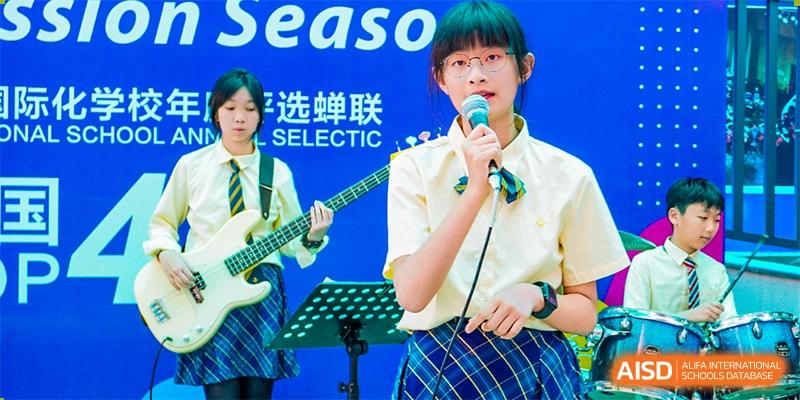 A female student from Guangdong Country Garden School in a plaid uniform sings into a microphone during a band performance.