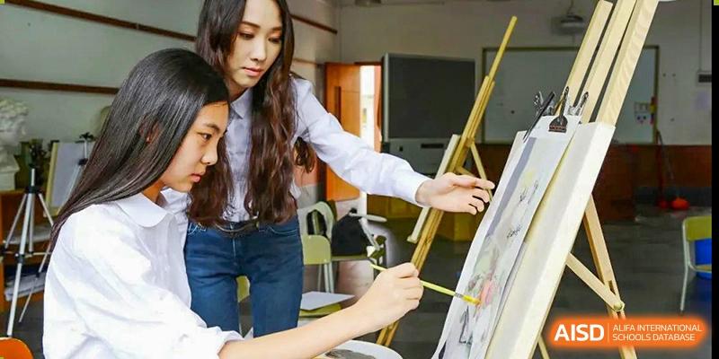 A female student from Guangdong Country Garden School in a white shirt paints on an easel in an art class.