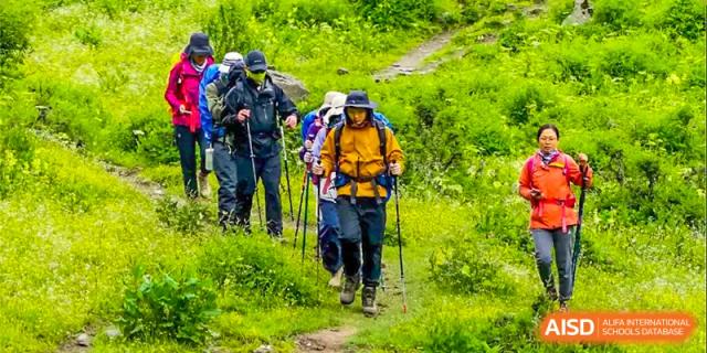 Two students from Guangdong Country Garden School with backpacks hike on a trail in a forest.