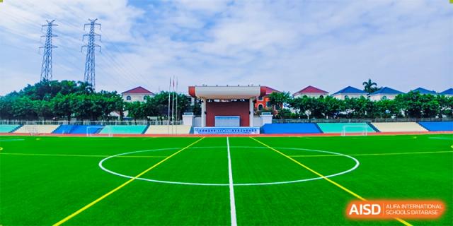 An exterior view of a school building at Guangdong Country Garden School with a green sports field and a red track.