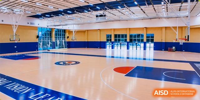A view of the indoor basketball court at Guangdong Country Garden School with a large, yellow basketball hoop.