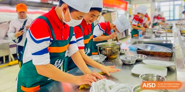 Students from Guangdong Country Garden School wearing chef's hats and masks learn how to prepare food in a cooking class.