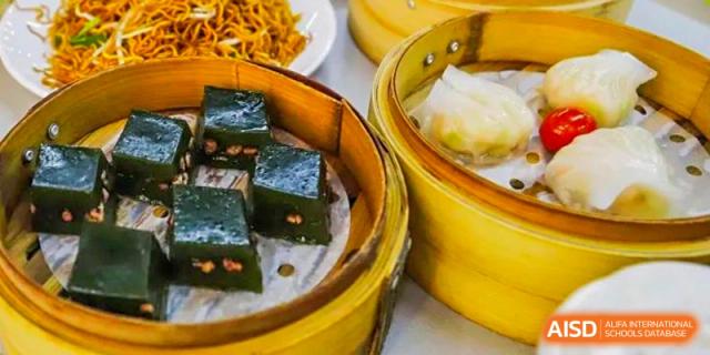 A close-up of a variety of steamed dim sum in bamboo baskets, part of a meal at Guangdong Country Garden School.