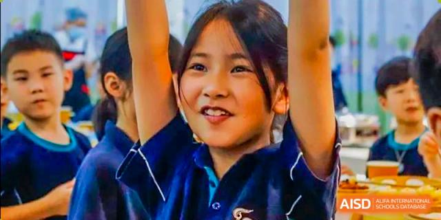A young female student from Guangdong Country Garden School in a blue shirt smiles with her hands raised high in the air.