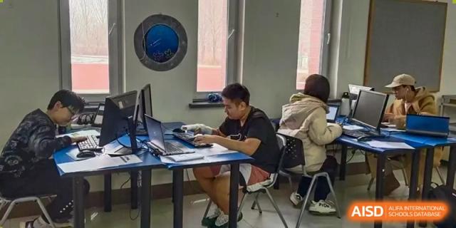 A male student is working on his laptop while others are around him at Shenyang International School.