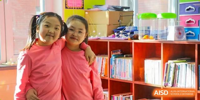 A young female student is smiling and standing in front of a bookshelf at Shenyang International School.