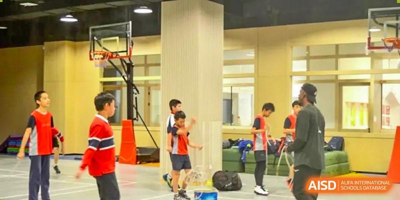 Four young students and an adult are playing badminton in a gym at Shenyang International School.