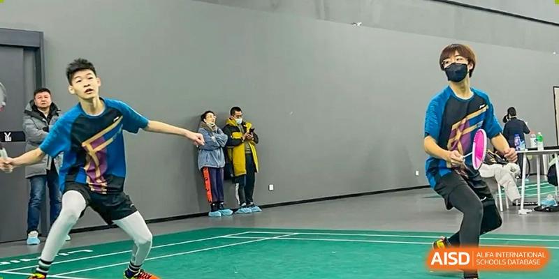 Two adults are standing and observing a badminton game at Shenyang International School.