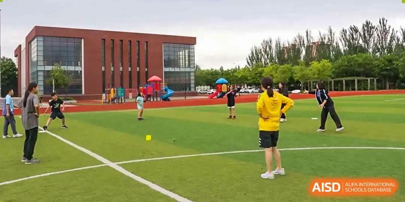 Students and a teacher are playing a game on a soccer field at Shenyang International School.