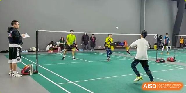 Two boys are playing badminton on a green court at Shenyang International School.