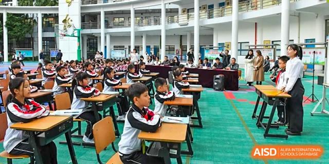 Shenzhen Yaohua Experimental School students seated at desks in an open area of the school, participating in an outdoor class or activity.