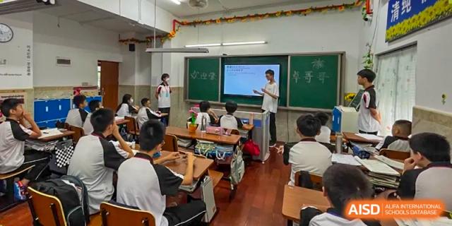 A male teacher at Shenzhen Yaohua Experimental School instructing students in a classroom with a combination of a chalkboard and a modern screen.