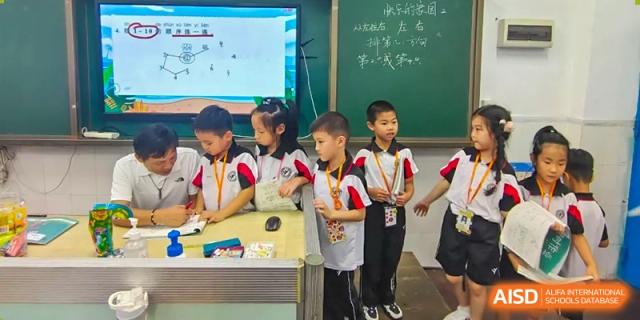 A small group of young students from Shenzhen Yaohua Experimental School standing proudly near a traditional green chalkboard in a classroom.