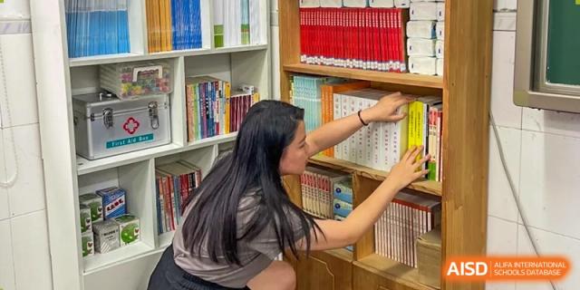 A female student from Shenzhen Yaohua Experimental School reaching to select a book from a shelf in the school library.