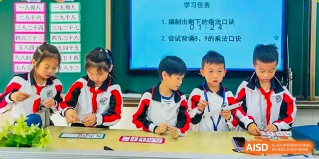 Two Shenzhen Yaohua Experimental School students presenting their work at a table in front of a large display screen during a class.