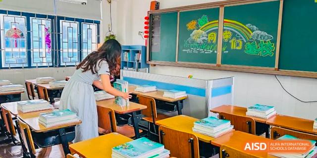 A female student from Shenzhen Yaohua Experimental School cleaning a traditional green chalkboard in a classroom.