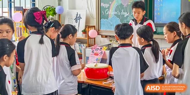 Shenzhen Yaohua Experimental School students celebrating Children's Day in a classroom, gathered around a small red drum and a cake.