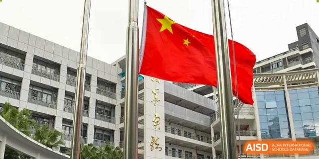 The Chinese national flag flying high in front of the modern academic buildings of Shenzhen Yaohua Experimental School.