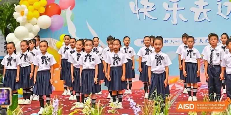 A group of younger female students from Shenzhen Yaohua Experimental School in uniform posing on a stage or platform.