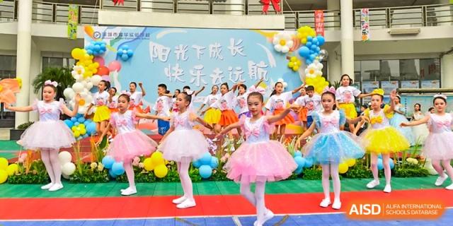 Young female students from Shenzhen Yaohua Experimental School performing a dance in white and pink tutus on a brightly decorated stage.