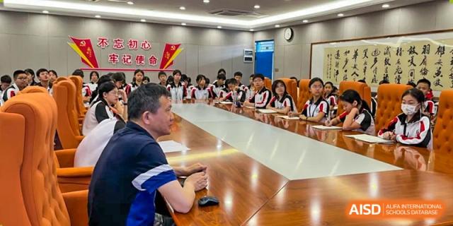 A meeting of Shenzhen Yaohua Experimental School staff and students seated around a large, polished wooden conference table.