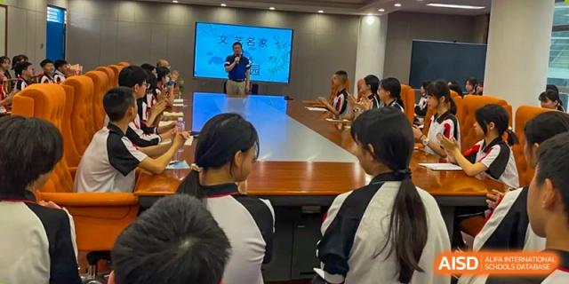 A male teacher at Shenzhen Yaohua Experimental School presenting a lesson to students in a conference room with a large screen display.