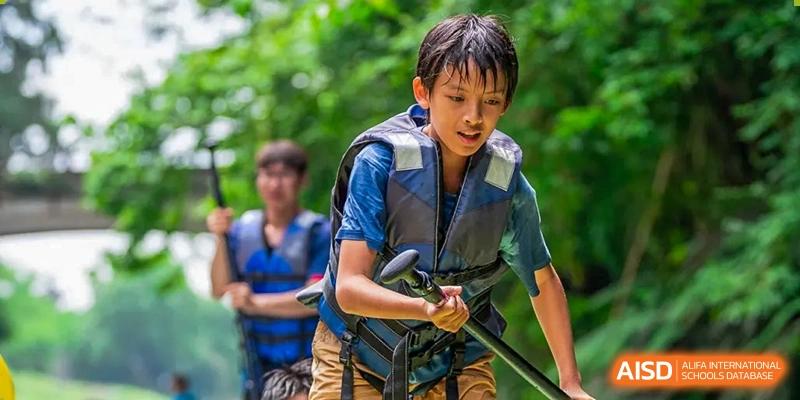 Two students from SPGS International School Chengdu participating in an outdoor activity, with one in the foreground wearing a life jacket and holding a paddle.