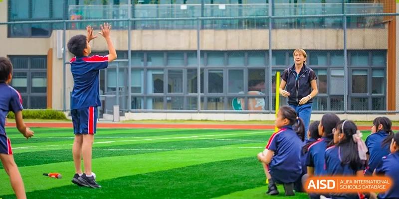 A close-up view of a green sports field with a student in red shorts running, SPGS International School Chengdu