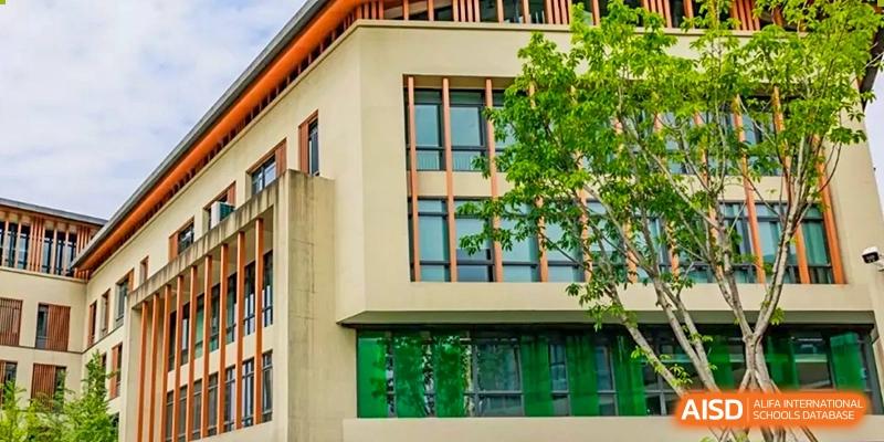 The modern exterior of a school building with large windows and surrounding greenery, SPGS International School Chengdu