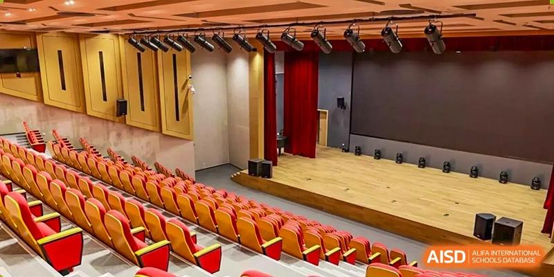 The interior of a school theater with rows of red seats and a stage, SPGS International School Chengdu