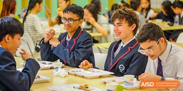 Two male students in school uniform smiling and eating lunch in a cafeteria, SPGS International School Chengdu