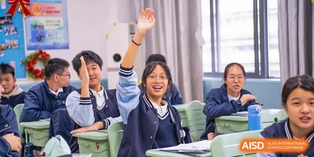 A student in a school uniform raising her hand in a classroom at Huzhou South Taihu Bilingual School.