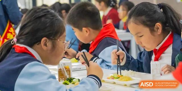 A group of young students eating a meal together in the cafeteria at Huzhou South Taihu Bilingual School.