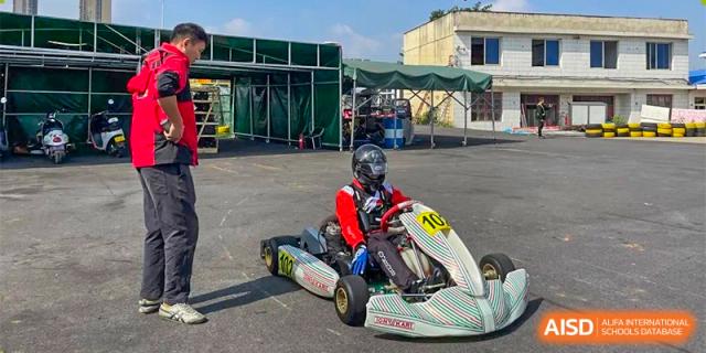 A student from The First High School of Changsha, Hunan driving a go-kart on an outdoor track, wearing a helmet and racing suit.