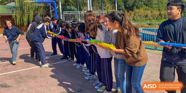 Students from The First High School of Changsha, Hunan participating in a team-building activity, passing an object down a line while holding ropes.