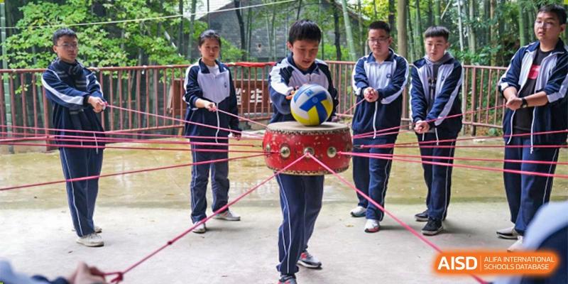 Students from The First High School of Changsha, Hunan engaging in a cooperative challenge, using strings to suspend and move a ball placed on a drum.