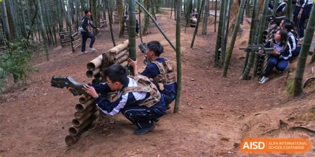Students from The First High School of Changsha, Hunan participating in a wilderness or outdoor survival-style activity among bamboo trees.