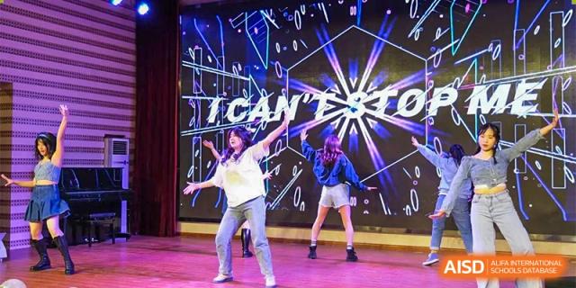 A student from The First High School of Changsha, Hunan performing a solo dance with others behind her on a stage featuring dynamic, colorful light graphics.
