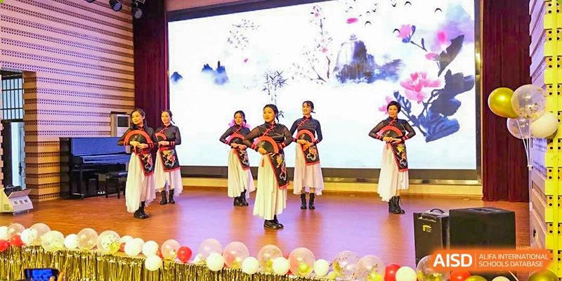 Students from The First High School of Changsha, Hunan performing a traditional cultural dance in ornate costumes on a stage decorated with balloons and a backdrop of blooming trees.
