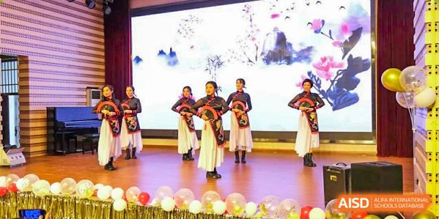 Students from The First High School of Changsha, Hunan performing a traditional cultural dance in ornate costumes on a stage decorated with balloons and a backdrop of blooming trees.