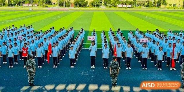 Students from The First High School of Changsha, Hunan lined up on a green sports field, possibly for military training or a school assembly, with an instructor facing them.